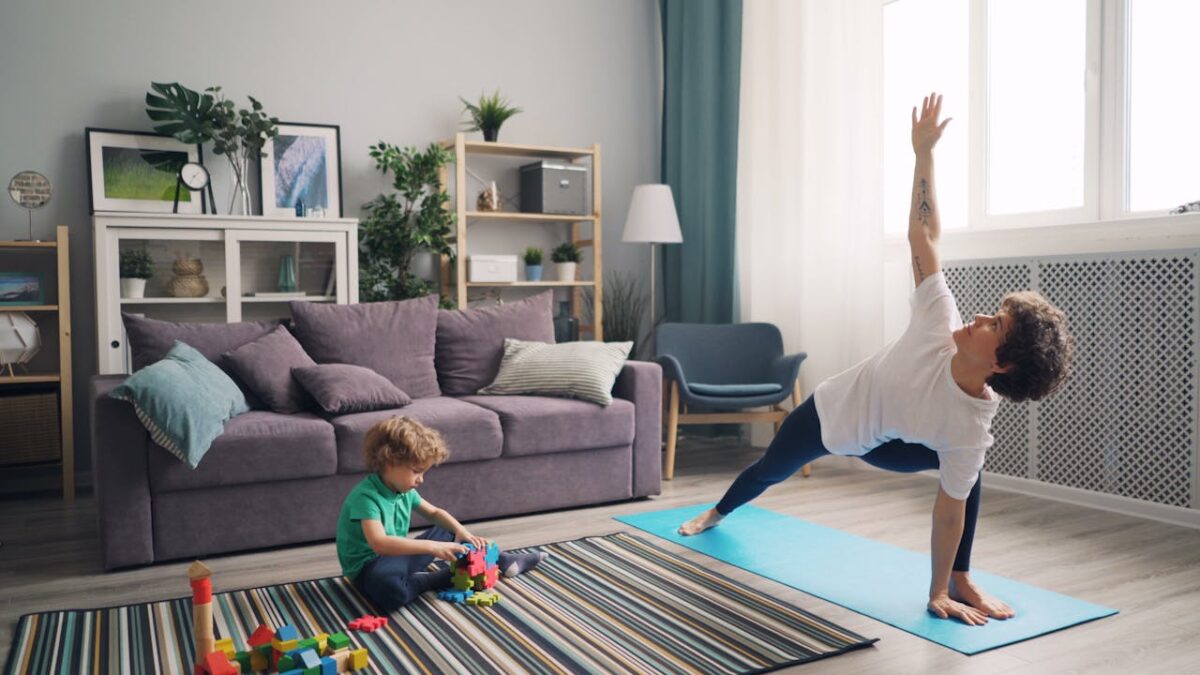 A woman does yoga on a mat as her child plays with colorful blocks in a cozy living room.