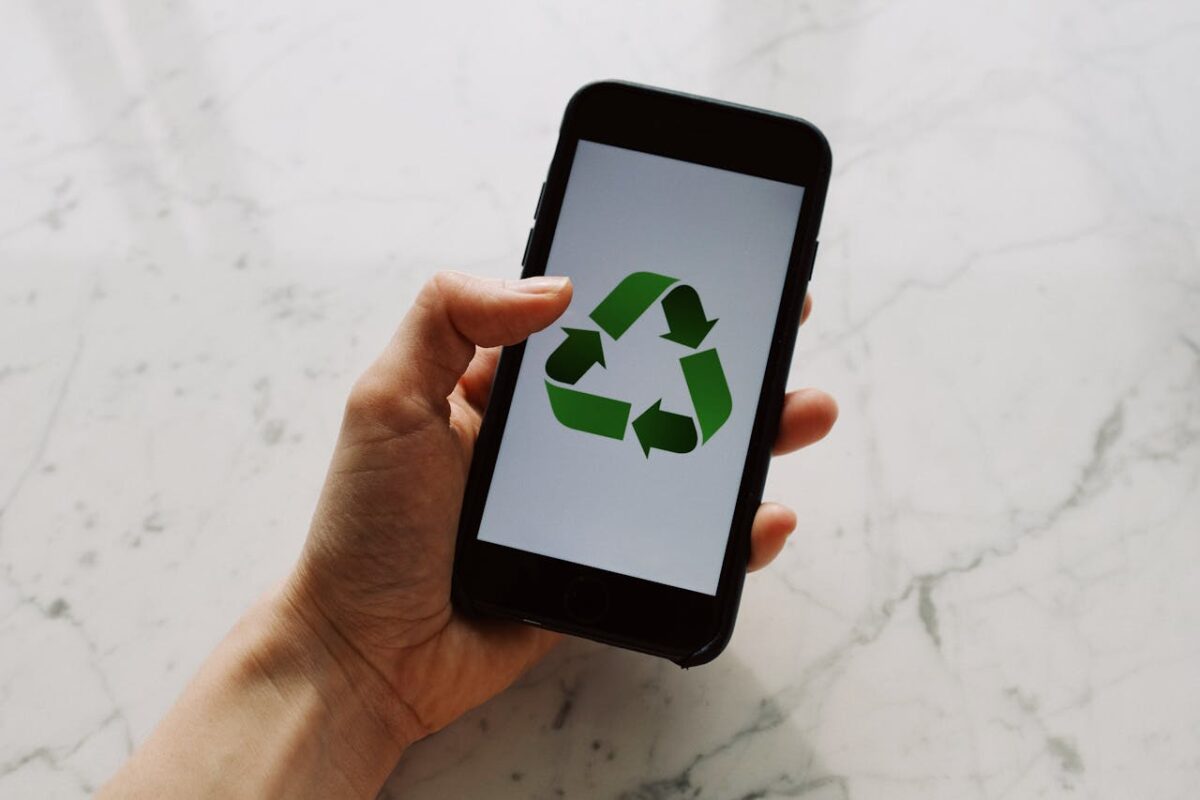 A close-up of a hand holding a smartphone with a recycling symbol on the screen, promoting sustainability and eco-consciousness.